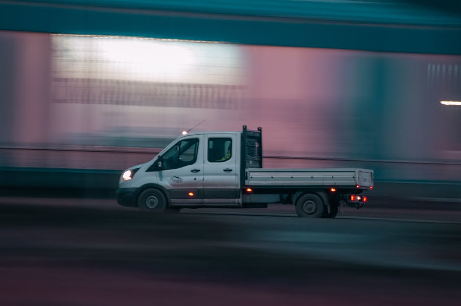 A white moving truck with its rear doors open, positioned on the street outside a commercial building, during daytime. The truck is part of a home relocation process managed by Roehampton Man and Van,